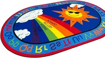 An oval carpet with a rainbow and a smiling sun wearing sunglasses at its centre, clouds beside it, and alphabet pairs around the blue border.