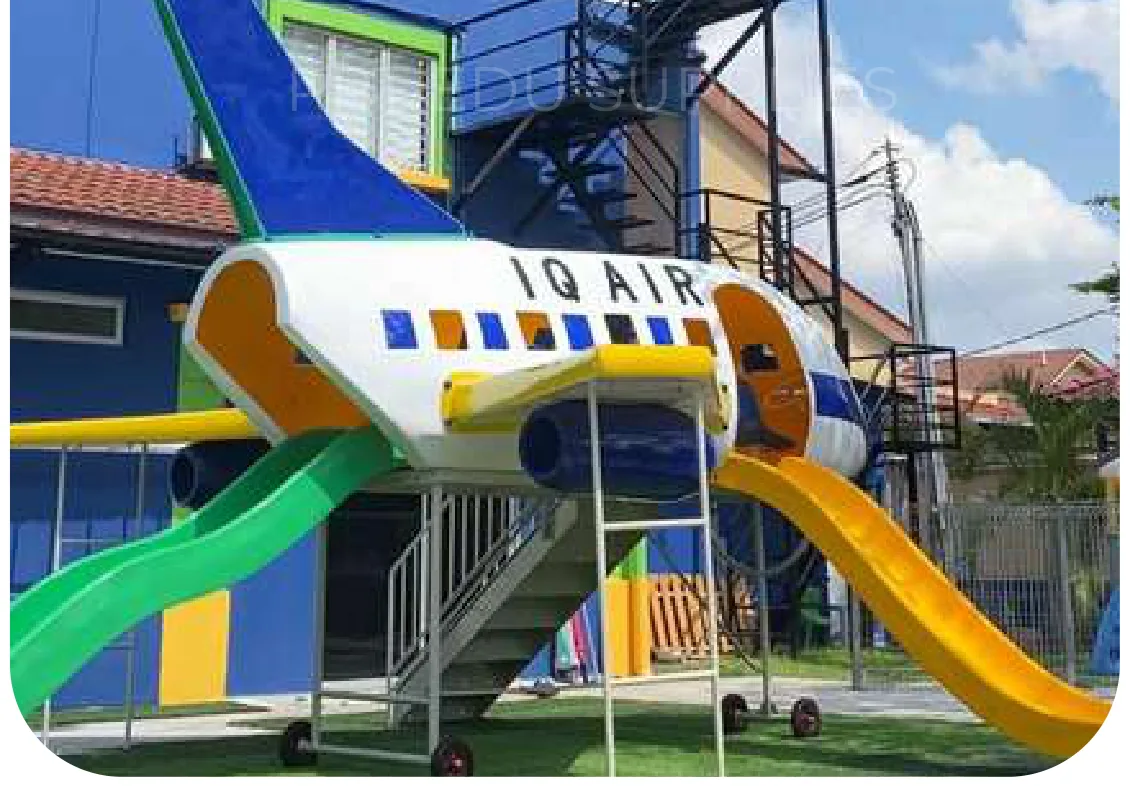 The aeroplane play unit installed outdoors, lettered IQ AIR, with a green slide from the door and a yellow slide at the tail.