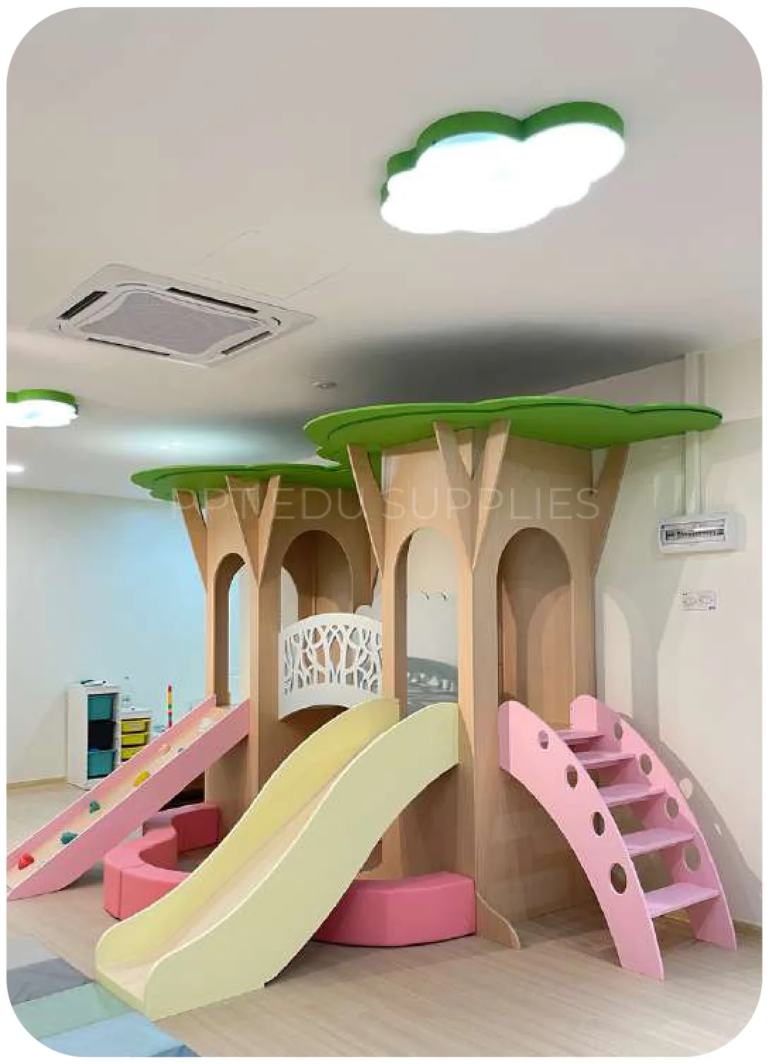 A timber play frame built around a tree trunk with a green canopy, a pink slide and a cream slide, on a pale wood floor.