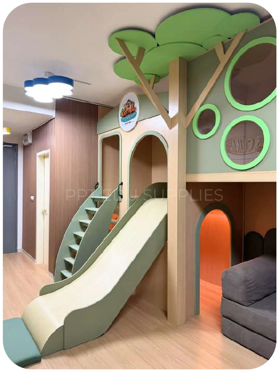 A timber tree frame with a green slide running down to a green padded landing, against a panelled wall.