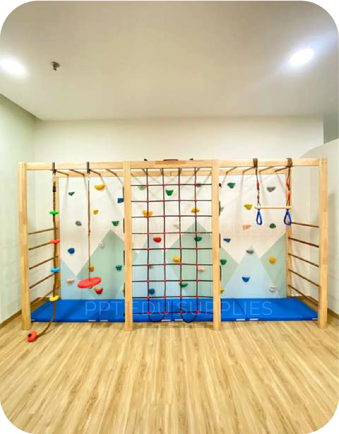 A freestanding timber frame across one wall carrying a cargo net, climbing holds, hanging rings and wall bars, over a blue landing mat.