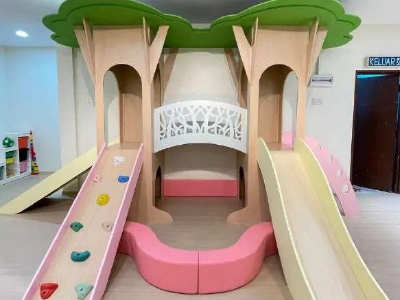 Plywood treehouse with green canopies, a pink climbing ramp, a cream slide and a curved pink bench on pale flooring.