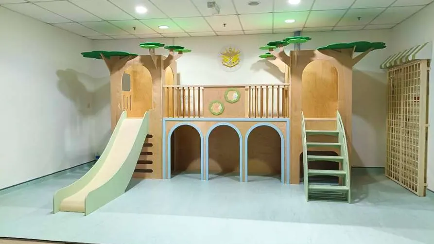 Indoor plywood treehouse on a raised platform, with green canopies, a mint slide and staircase, and arched openings below.