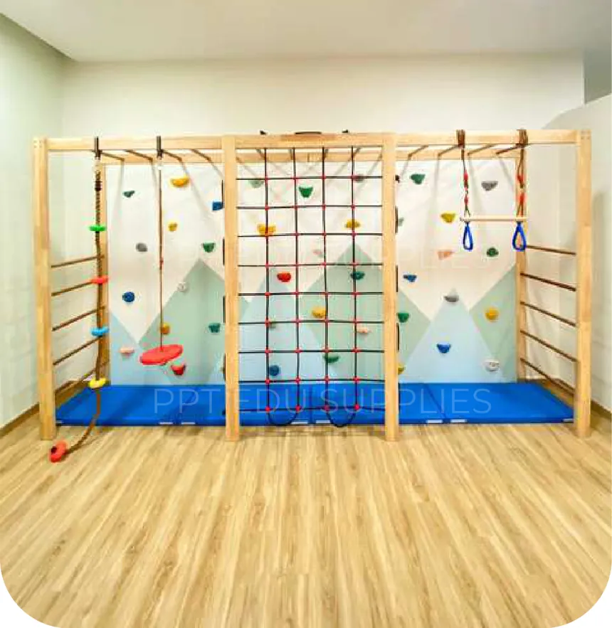 A freestanding timber frame across one wall of
      the same room, carrying a cargo net, climbing holds, hanging rings and wall bars,
      over a blue landing mat on a wood floor.