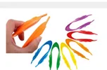 Eight long plastic tweezers in eight colours, one held in a hand.