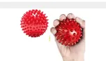 Two red spiked massage balls, one held in a hand.
